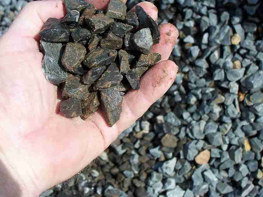 A hand holding angular crushed-stone aggregate above a gravel pile.