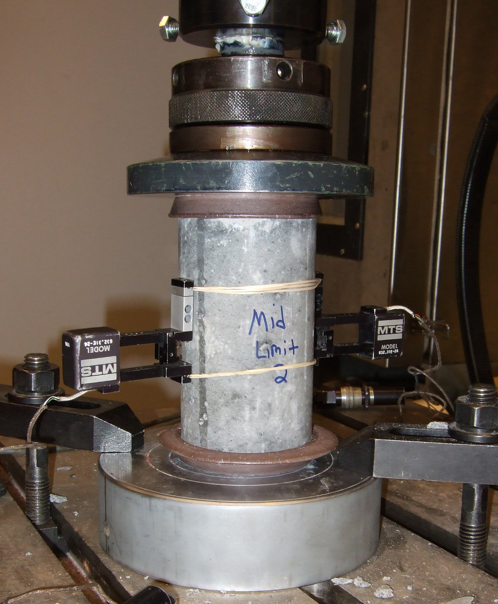 A lightweight concrete cylinder held between the platens of a laboratory compression-testing machine.