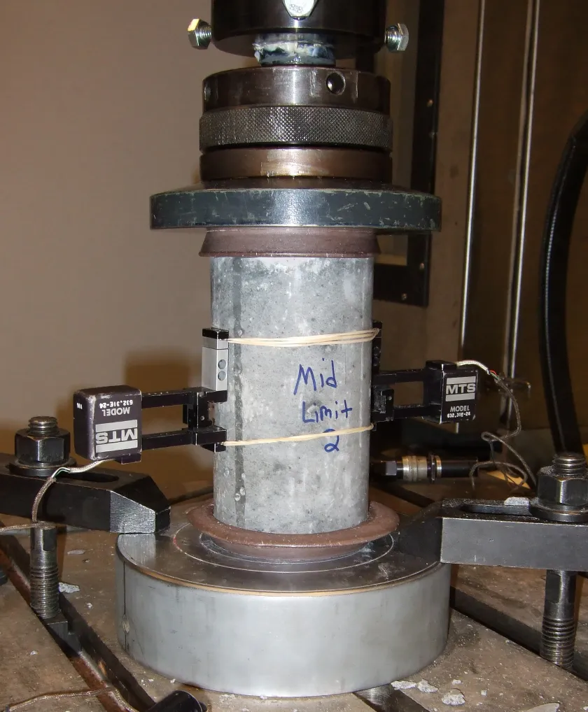 A lightweight concrete cylinder held between the platens of a laboratory compression-testing machine.